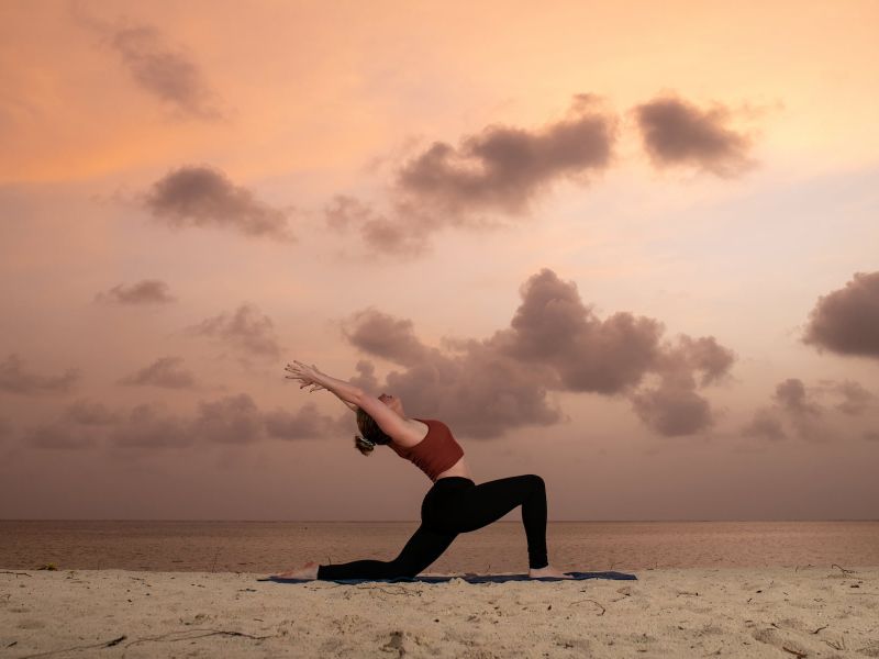 Silhouette einer Frau, die Yoga im Sand bei Sonnenaufgang praktiziert