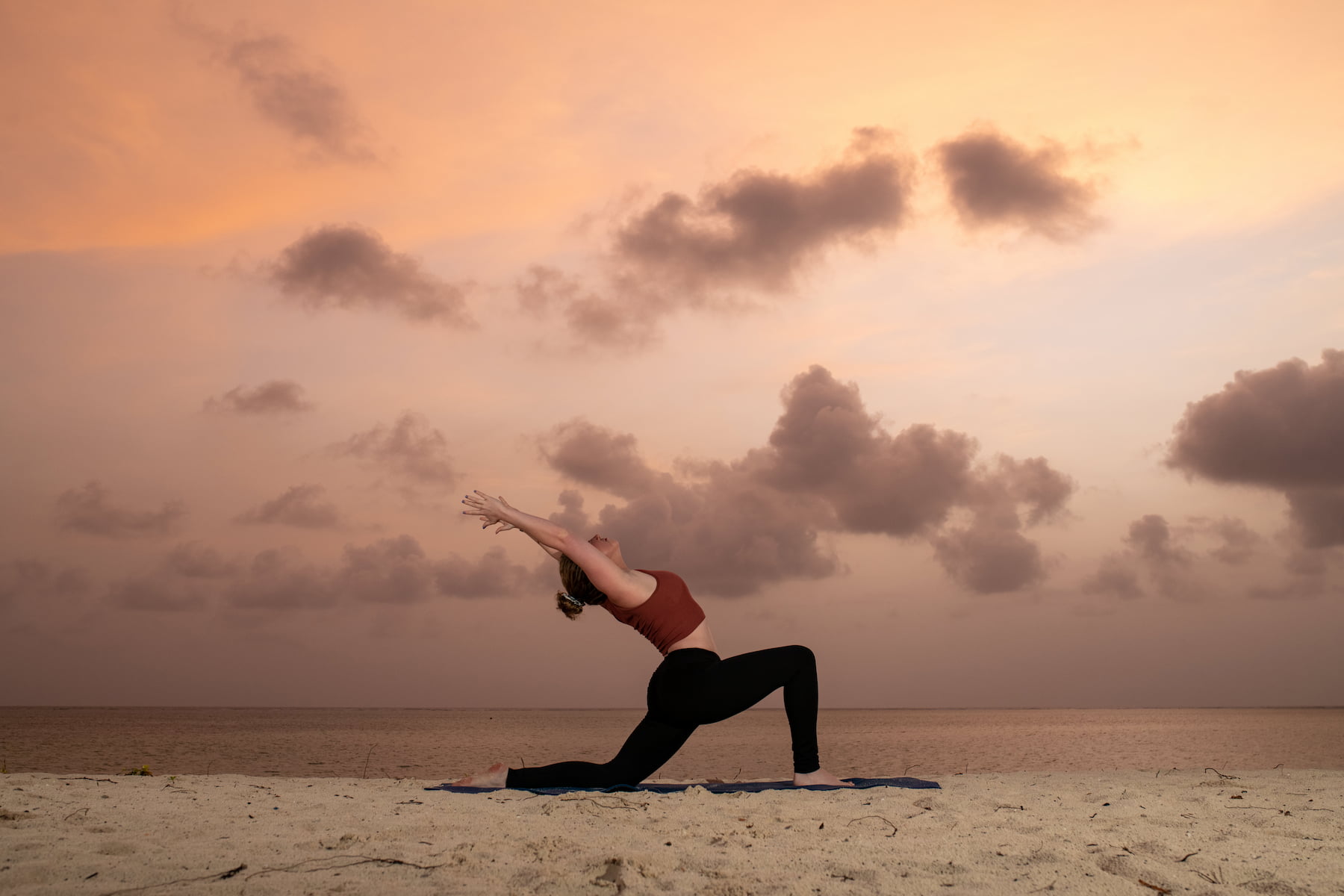 Silhouette einer Frau, die Yoga im Sand bei Sonnenaufgang praktiziert