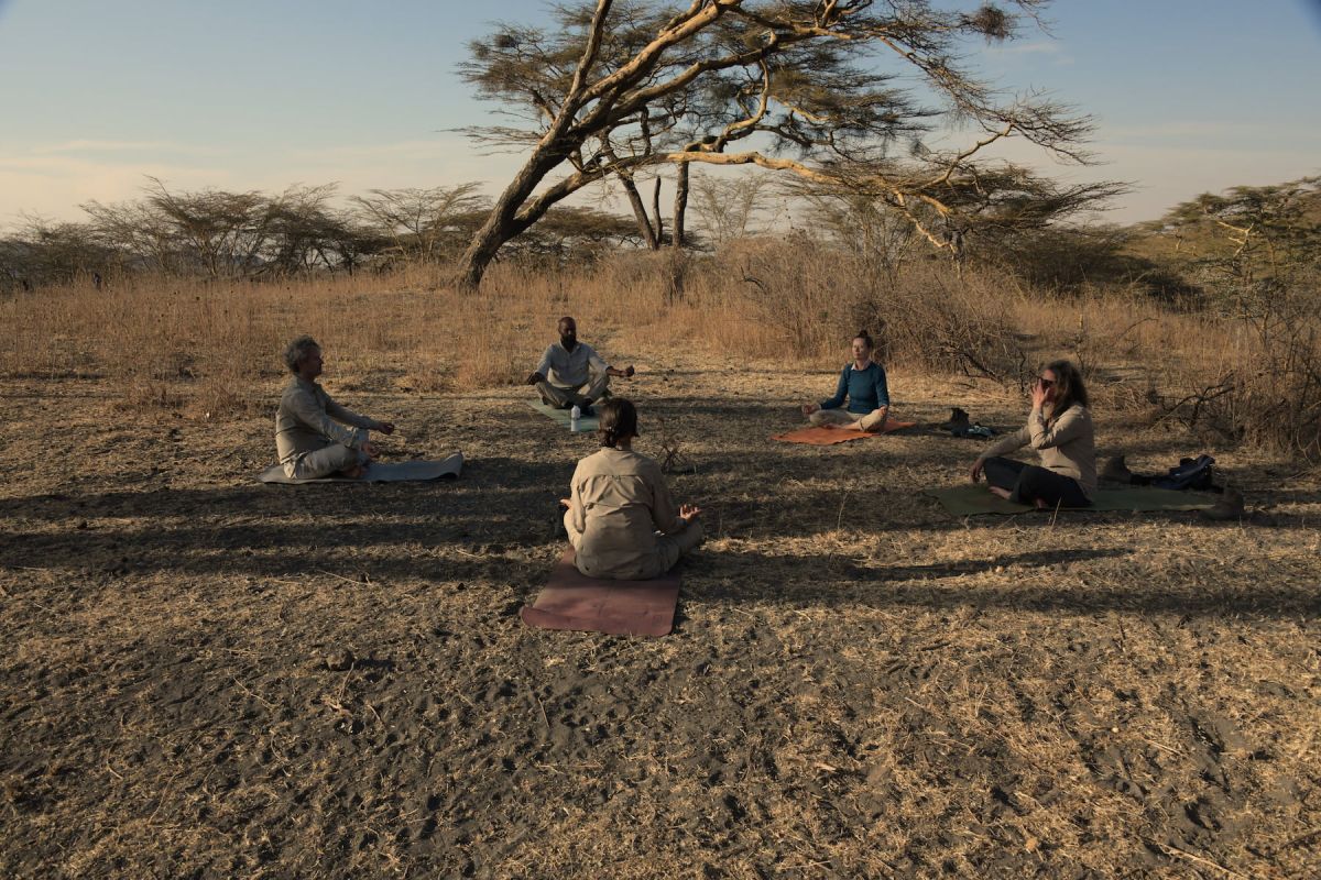 Gruppe sitzt im Kreis und macht Yoga-Übungen in der freien Natur Tansanias