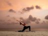 Silhouette einer Frau, die Yoga im Sand bei Sonnenaufgang praktiziert